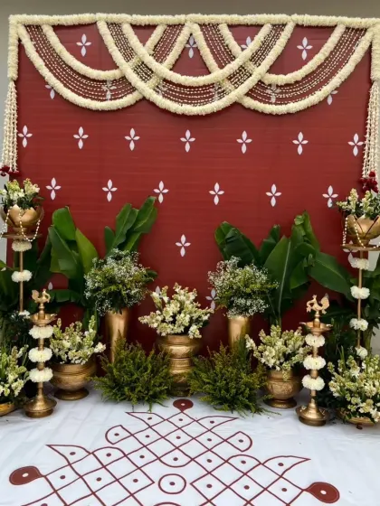 The full view of the traditional red backdrop with a hand-drawn rangoli on the floor. The setup is completed with banana plants and brass lamps, perfect for any auspicious occasion.