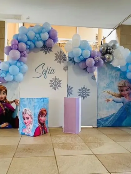 A beautiful outdoor Frozen party setup for Sofia's 5th birthday. The decor includes a balloon arch in wintery colors, character backdrops, and a large light-up marquee number '5'.
