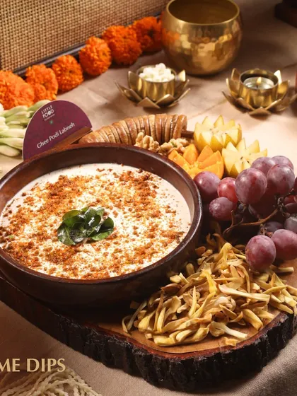 A close-up of our Ghee Podi Labneh, a fusion dip that combines South Indian spices with creamy yogurt. Served on a rustic wooden platter with fruits and crisps, it's a unique highlight of our Indian grazing table.