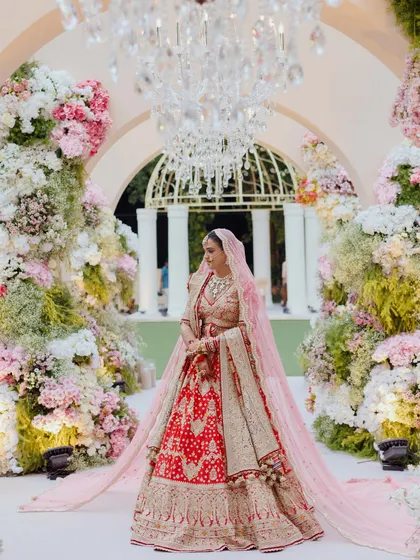 The bride in all her glory, standing amidst the stunning floral decor. This full-length shot shows how the entire look, from the long veil to the perfectly draped lehenga, creates a breathtaking bridal entry.