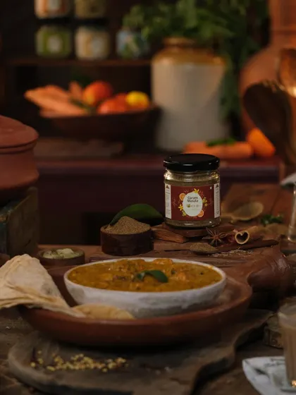 A rustic dining scene with a bowl of dal and a jar of sambar masala. This food styling places the product in the context of a delicious, home-cooked meal.