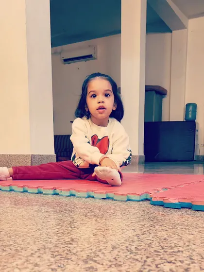 Even our tiniest gymnasts learn foundational poses. This little one is practicing a seated split stretch, an important step in developing the flexibility required for more advanced gymnastics skills later on.