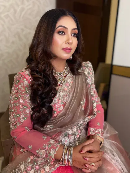 The makeup is soft yet defined, enhancing her features beautifully. The pink and grey saree is complemented by the warm tones on her eyes and lips.
