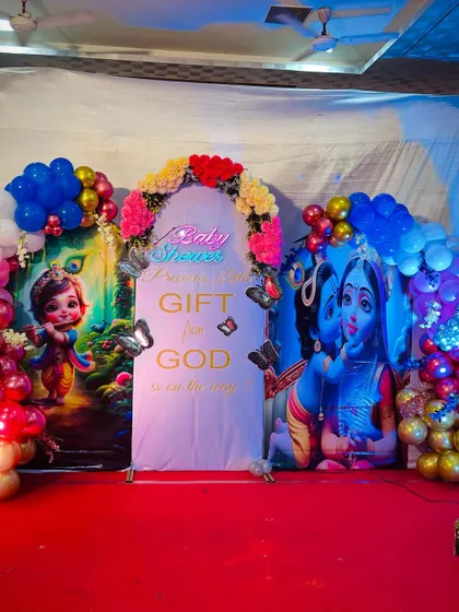 A clear shot of the central backdrop for the Krishna themed baby shower. It features a neon sign, butterfly accents, and a message that reads 'A precious little gift from God is on the way'.