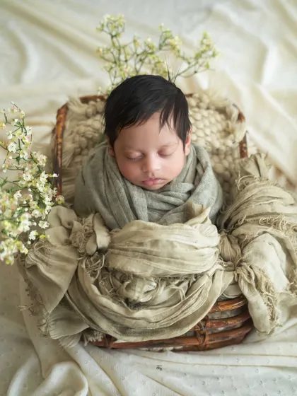 This baby boy is nestled in a rustic basket with soft, neutral green and beige wraps. The delicate white flowers add a touch of lightness.