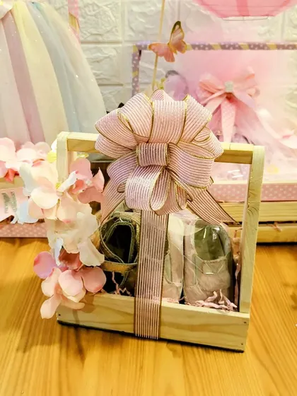 A detail shot of a wooden crate hamper created for a baby girl's arrival. The large, striped bow and floral accents add a touch of sweetness to the curated gifts inside.