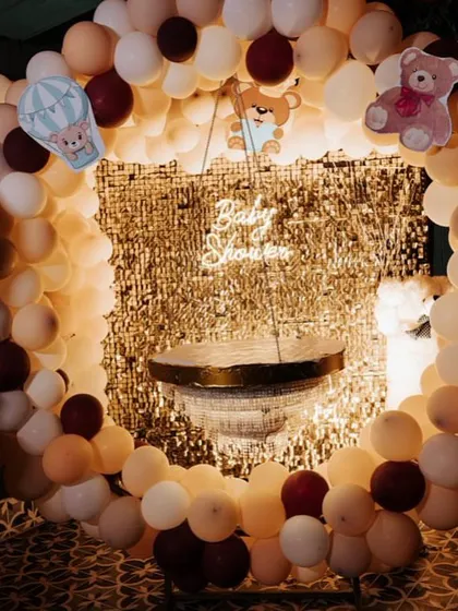 A teddy bear-themed baby shower with a warm and cozy feel. The decor features a circular balloon arch in neutral tones against a gold shimmer wall.