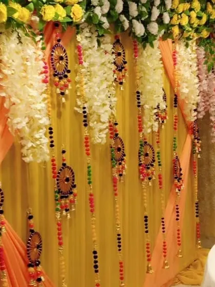 A close-up of a decorated backdrop showing hanging floral strings and traditional ornaments against a yellow drape.