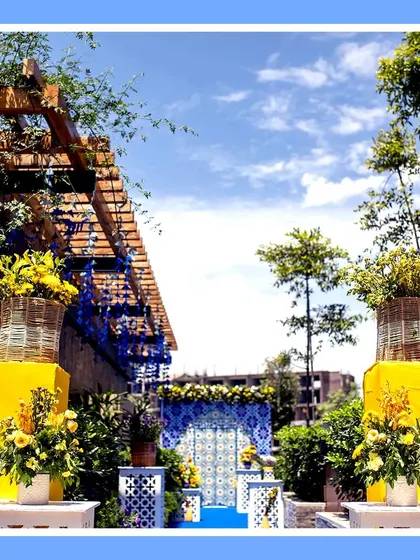 A vibrant Haldi entrance combining the royal blue of Jodhpur with the sunny yellow of marigolds. The setup features a floral arch and a walkway lined with flowers, creating a stunning visual contrast.