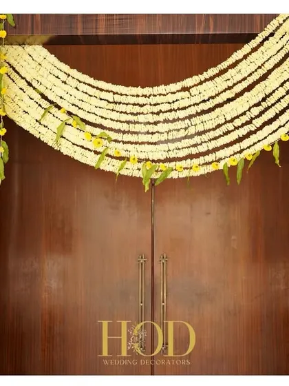 A simple yet beautiful floral decoration for a doorway. A thick garland of jasmine flowers creates a traditional and fragrant welcome, perfect for a home-based ceremony or an intimate event.