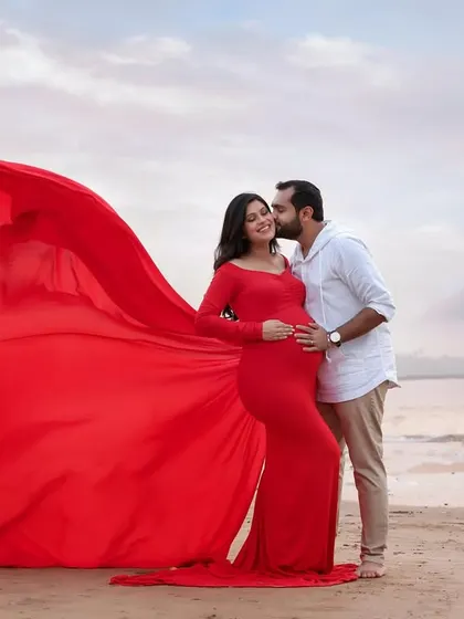 A tender kiss from the dad-to-be, as the vibrant red gown flows in the wind. This shot combines romance and drama for a stunning outdoor maternity portrait.