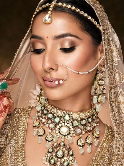 A classic bridal pose, with the hand gently touching the face. This gesture highlights the henna design and the large emerald ring, while the downward gaze creates a sense of demure elegance.