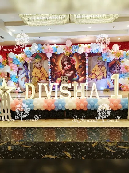 A grand stage for a Krishna-themed first birthday, with beautiful imagery of Little Krishna, pastel balloon decorations, and large marquee letters.