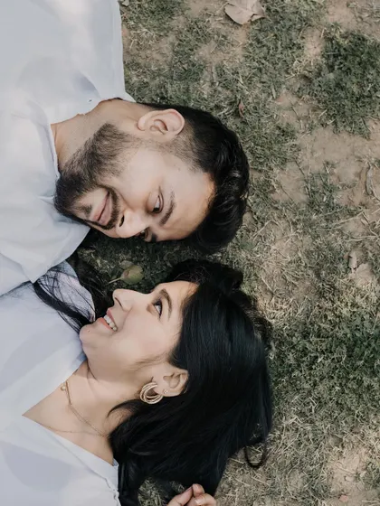 An aerial view of a couple lying on the grass, looking at each other with smiles. This creative angle offers a unique and intimate perspective on their connection.