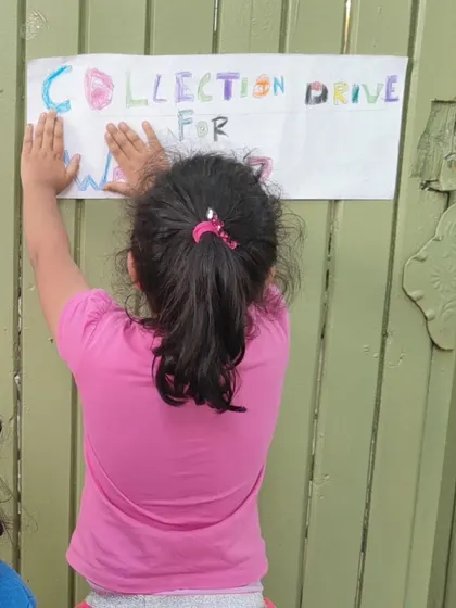 A child proudly puts up a handmade poster for the Wayanad collection drive, taking ownership of the initiative.