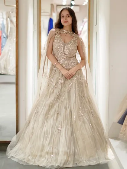 A full, poised shot of the beige gown with its elegant cape. The high neckline and flowing tulle create a look that is both regal and modern, ideal for an engagement ceremony.