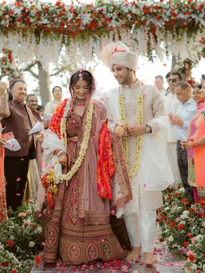 The couple walks together after their wedding ceremony, surrounded by family and a shower of petals. A perfect candid moment of happiness.