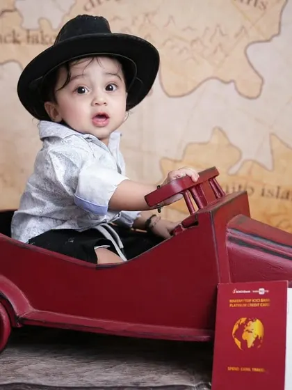 A curious little traveler looks on during his adventure-themed photoshoot, sitting in a vintage-style toy car.