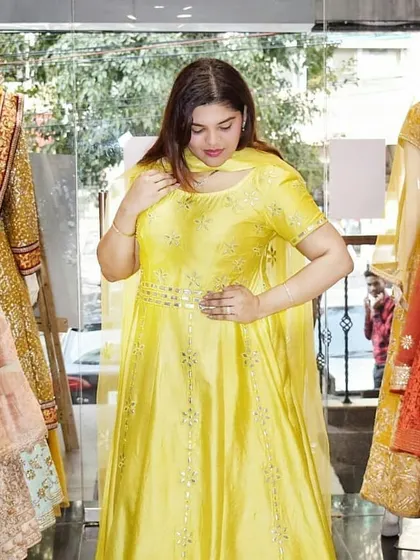 A client admiring a bright yellow Anarkali suit in the store. This cheerful color is perfect for a Haldi or Mehendi ceremony.