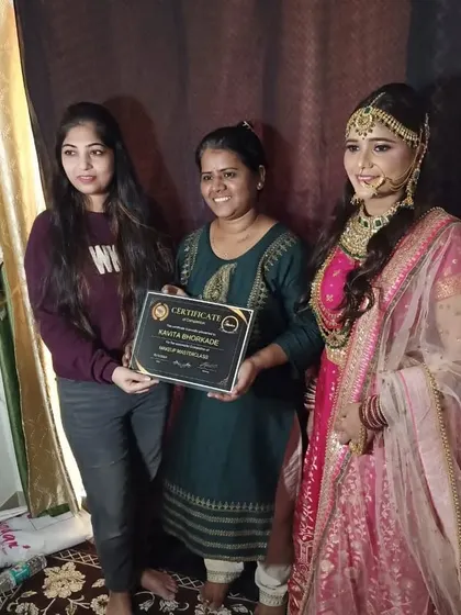 A student receives her makeup workshop certificate next to a model showcasing a full bridal look.