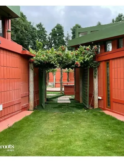 An inviting entryway is created by a lush green path leading through an archway covered in flowering vines. The distinctive red-tiled walls of the farmhouse provide a warm and striking contrast to the verdant landscape.