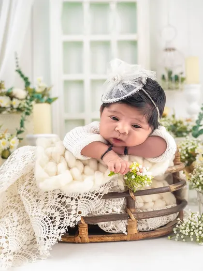 A precious awake moment! This baby peeks over the edge of a basket, surrounded by a beautiful arrangement of white and cream flowers.