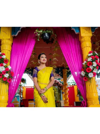 A portrait of the bride in a vibrant yellow saree, standing under a colorful mandap.