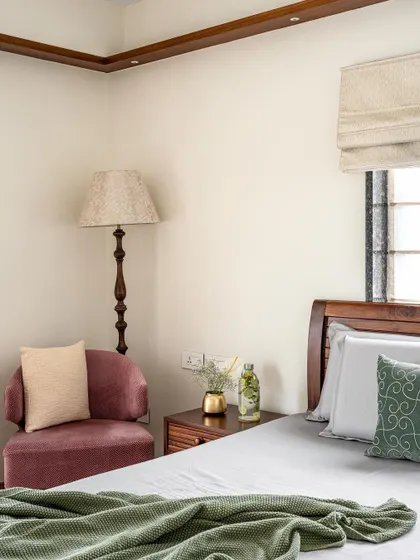 The parent's room in 'Gulmohar' maintains a consistent theme of warm wood and neutral tones. A cozy armchair in the corner creates a comfortable reading spot.