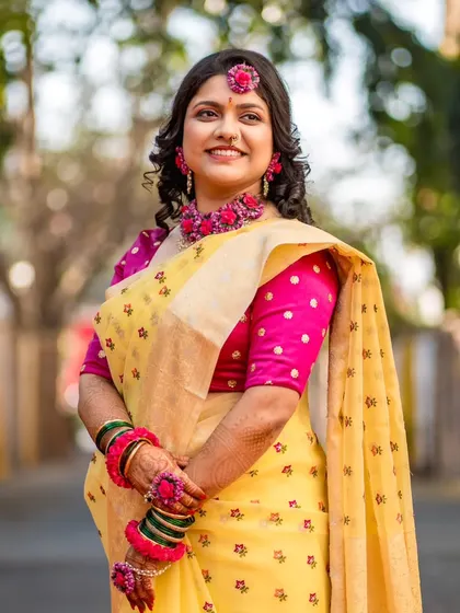 A classic outdoor portrait of the bride in her yellow Haldi ceremony attire, adorned with beautiful floral jewelry.