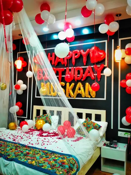 A clear shot of the "Happy Birthday Muskan" bedroom decoration, with the bed canopy, foil balloons, and petals all beautifully arranged.