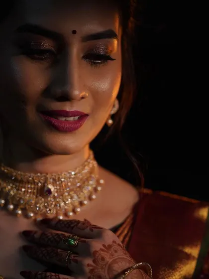 A dramatic and beautiful portrait of a bride in a deep red silk saree. The makeup is focused on glowing skin and a rich lip color, creating a sophisticated look for her reception.