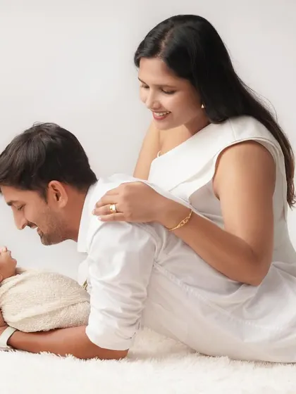 A relaxed and loving pose with mom and dad admiring their newborn baby. The simple white outfits and soft rug create a clean, timeless family portrait.