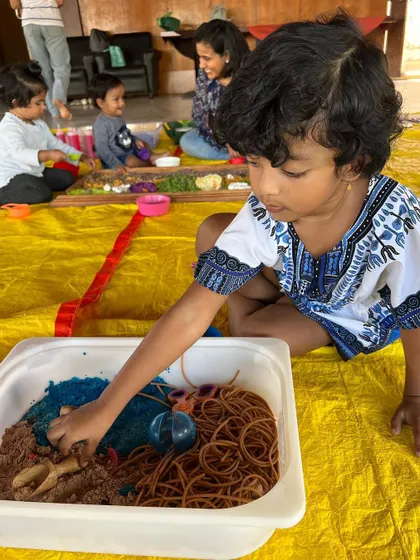 This child is exploring a sensory bin with different textures, including sand, cooked spaghetti, and water beads. Mixing and matching materials is a key part of child-led discovery.