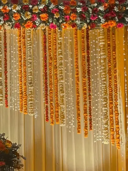 Another angle of the cascading marigold and tuberose floral curtain. The warm yellow tones of the backdrop fabric complement the flowers, creating a bright and auspicious atmosphere.