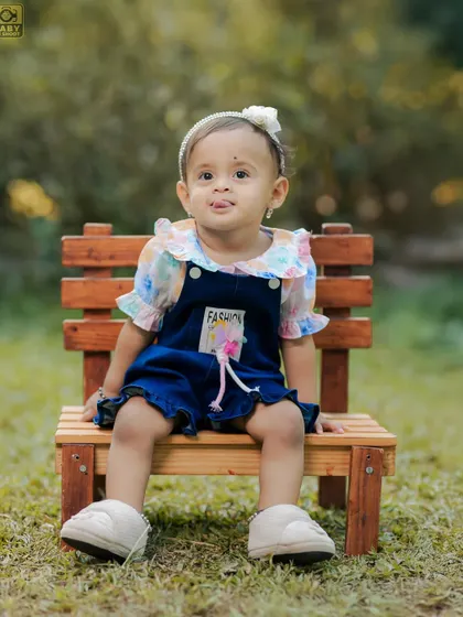 A cute portrait of a little girl sitting on a bench in the park, with a sweet, curious expression.