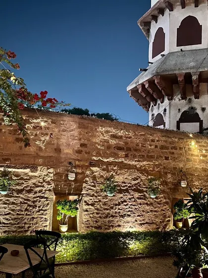 An evening view of a courtyard in Jodhpur, with soft lighting on the textured stone walls and hanging plants. This is a perfect example of how to use lighting and greenery to create a peaceful and beautiful outdoor or semi-outdoor space.