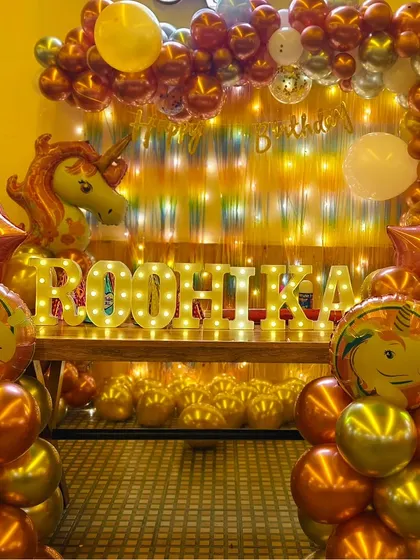 A full view of the unicorn-themed first birthday decor for Roohika, showing the beautiful combination of chrome balloons, a shimmer curtain, and marquee letters.
