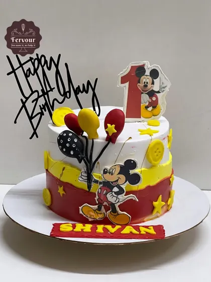 A classic Mickey Mouse cake for a first birthday celebration. The design features Mickey's signature colors of red, yellow, and black, along with cute balloon details and a fun topper.