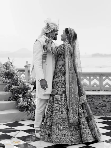 A classic black and white portrait of the couple on their wedding day in Udaipur, with the serene lake and City Palace in the background.
