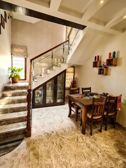 This image shows how I utilize space efficiently by placing a compact dining set adjacent to the staircase. The area under the stairs is converted into a custom wooden crockery and storage unit with glass doors, blending functionality with the home's aesthetic.