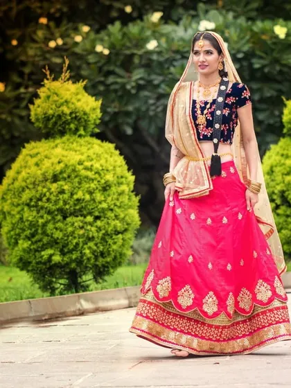 Inspired by the divine stories of Radha, this custom lehenga features a bright pink skirt with a gold border and a contrasting navy blue embroidered blouse. It's a beautiful choice for festive occasions or pre-wedding ceremonies.