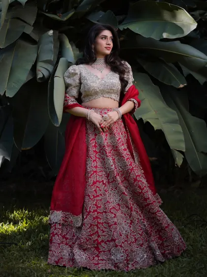 The magnificent Mahima in a stunning red and gold lehenga. Her makeup is soft and radiant, with a neutral lip and defined eyes that complement the rich colors of her outfit.