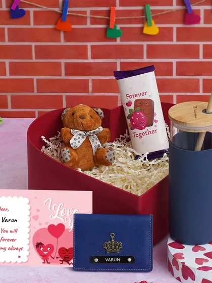 This "Love Keepsake Hamper" for him comes in a heart-shaped box. It features a personalized glass tumbler, a mini wallet in blue, a teddy bear, chocolate, and a custom message card.