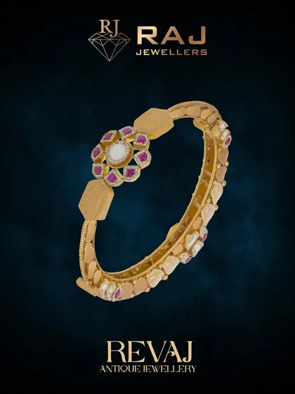 This elegant Revaj bangle features a central floral medallion set with a polki stone and rubies. The band itself has a unique, textured design, making it a beautiful statement of antique craftsmanship.