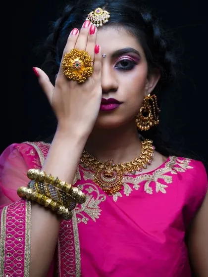 A creative pose from a bridal portfolio shoot, focusing on the dramatic pink eye makeup and traditional gold jewelry.