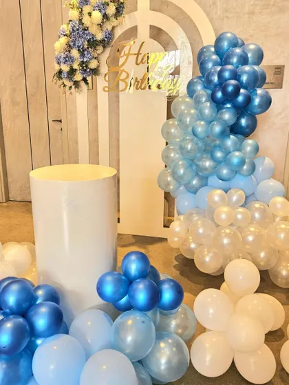 For a stylish 12th birthday, we designed this modern and chic setup. It features a cool blue and white balloon arrangement, a layered arch backdrop, and clean white plinths for a sophisticated party look.