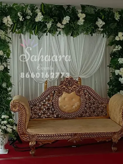 A lush green floral arch provides a beautiful frame for this engagement stage. The simple white drapery and classic gold-trimmed sofa create a look of natural elegance.