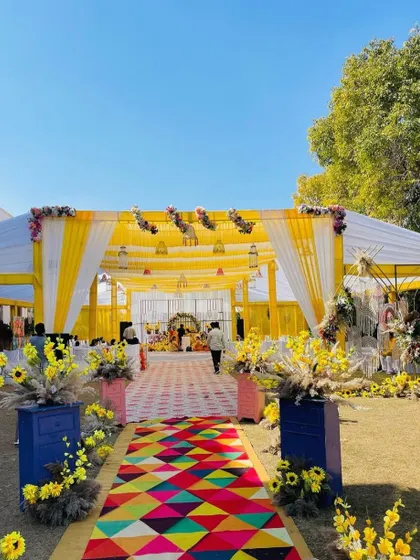 The entrance to a vibrant Haldi ceremony, featuring a colorful geometric-patterned aisle runner that adds a modern and fun element to the traditional yellow decor.