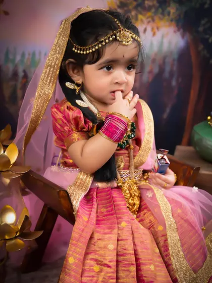 A beautiful little girl dressed as Radha, looking thoughtful and sweet. The rich pink and gold of her traditional dress are absolutely stunning.