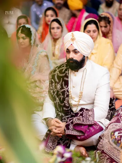 A candid shot of the groom during the Anand Karaj, listening intently to the Gurbani. The focus is on his respectful and serene demeanor.